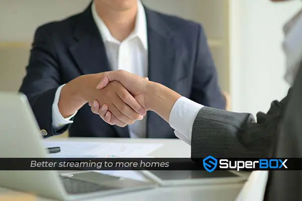 Business partners shake hands in a professional setting, symbolizing a deal for SuperBox's streaming services expansion.